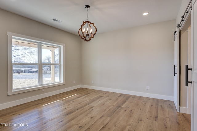 unfurnished room with a barn door, a notable chandelier, and light hardwood / wood-style flooring