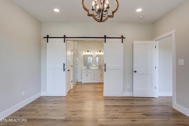 unfurnished bedroom featuring connected bathroom, light hardwood / wood-style flooring, a barn door, and a chandelier