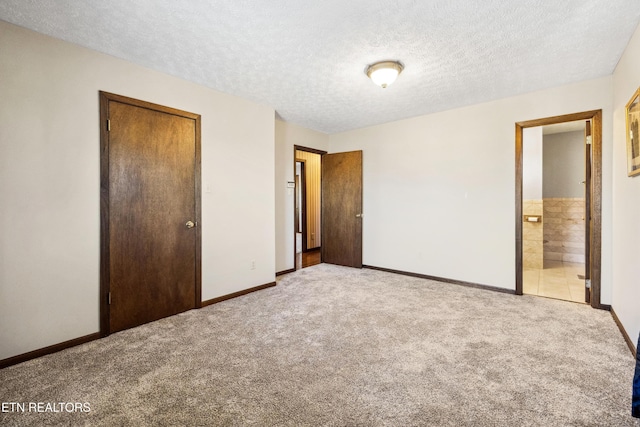 unfurnished bedroom featuring light colored carpet, connected bathroom, a closet, and a textured ceiling