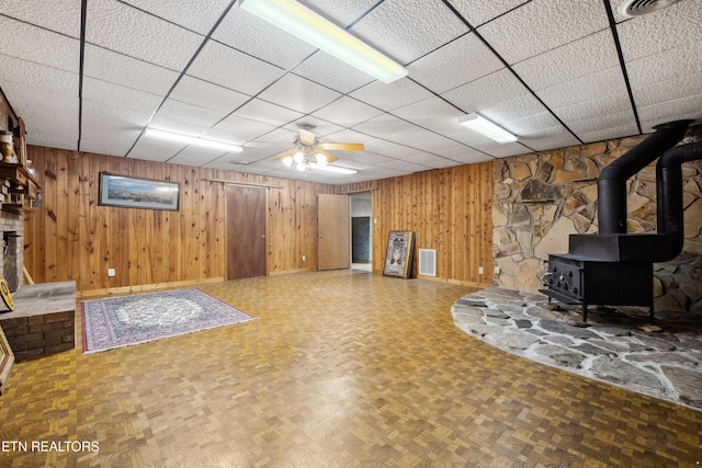 basement featuring parquet flooring, wood walls, and a wood stove