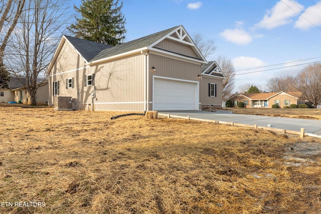 view of side of home with an attached garage, cooling unit, and concrete driveway