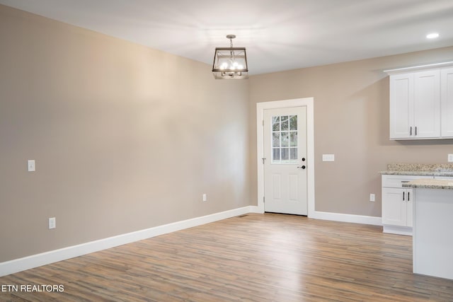 unfurnished dining area featuring baseboards, recessed lighting, wood finished floors, and a notable chandelier