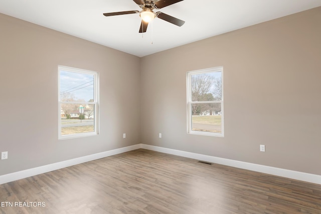 spare room featuring baseboards, ceiling fan, wood finished floors, and visible vents