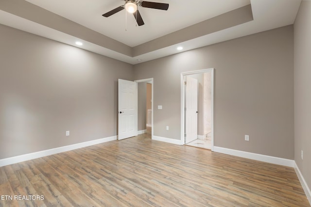 empty room with baseboards, ceiling fan, recessed lighting, a raised ceiling, and light wood finished floors