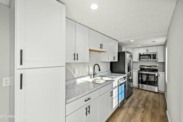 kitchen featuring sink, appliances with stainless steel finishes, wood-type flooring, light stone countertops, and white cabinets