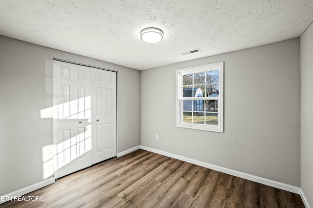 unfurnished bedroom featuring wood-type flooring, a closet, and a textured ceiling