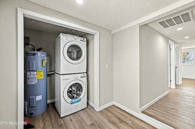 clothes washing area featuring stacked washer and clothes dryer, water heater, and light wood-type flooring