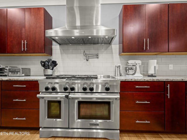 kitchen featuring light stone counters, double oven range, decorative backsplash, and range hood