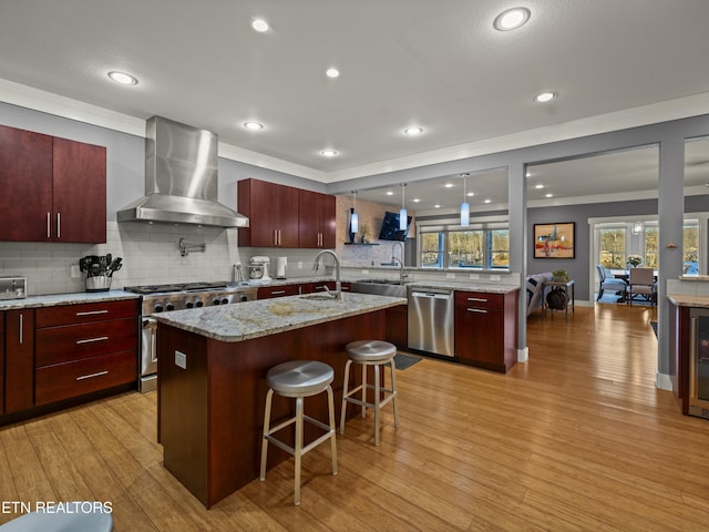 kitchen featuring appliances with stainless steel finishes, ventilation hood, an island with sink, a kitchen breakfast bar, and crown molding