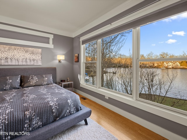 bedroom with crown molding, wood-type flooring, and a water view