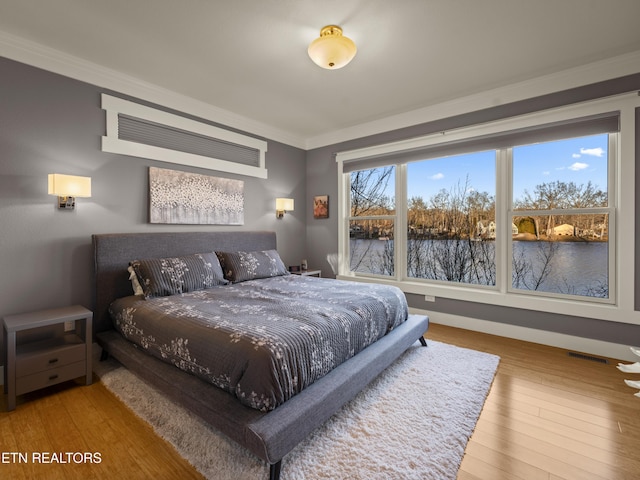 bedroom featuring crown molding, wood-type flooring, and a water view