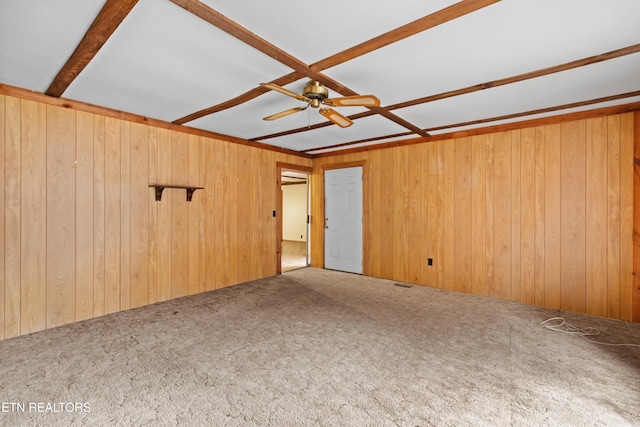 spare room featuring carpet floors, ceiling fan, and wood walls