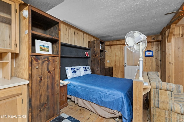 bedroom featuring wooden walls, light hardwood / wood-style floors, and a textured ceiling