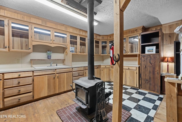 kitchen with wood walls, a wood stove, sink, light wood-type flooring, and a textured ceiling