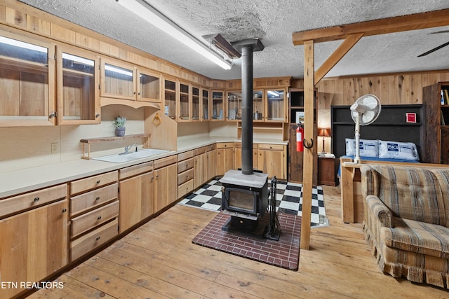 kitchen featuring sink, light hardwood / wood-style flooring, a wood stove, a textured ceiling, and wood walls