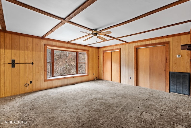 unfurnished bedroom with two closets, wood walls, ceiling fan, and carpet