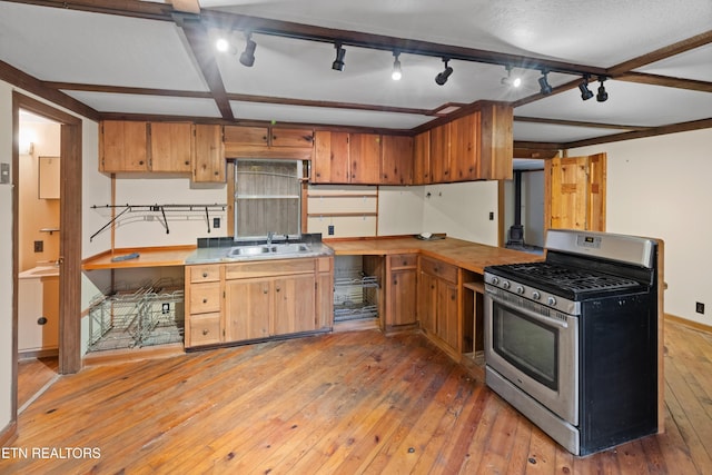 kitchen with beam ceiling, stainless steel gas range, sink, and light hardwood / wood-style flooring