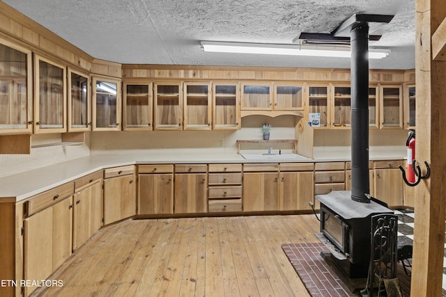 kitchen featuring sink, a wood stove, a textured ceiling, and light hardwood / wood-style floors