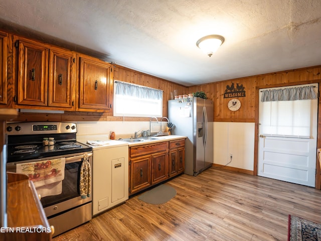 kitchen with stainless steel appliances, sink, light hardwood / wood-style floors, and wood walls