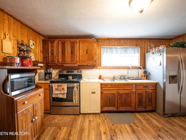 kitchen featuring sink, stainless steel appliances, wood walls, and light wood-type flooring