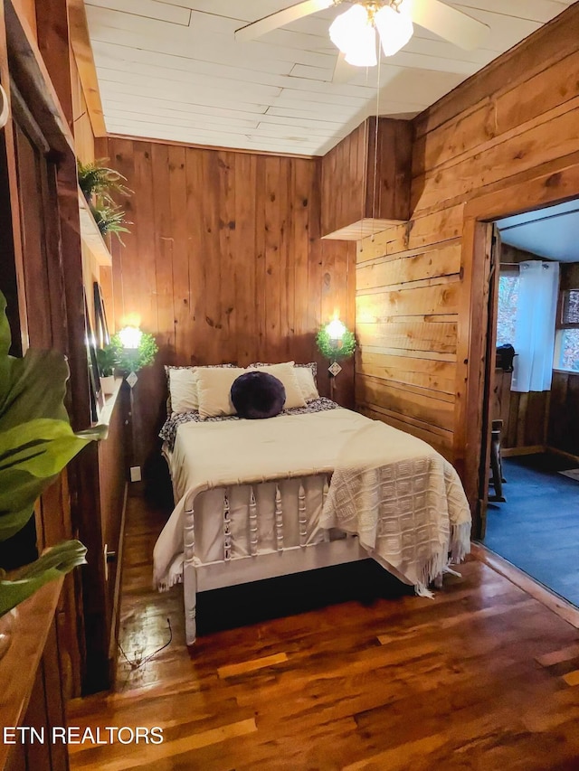 bedroom featuring ceiling fan, dark wood-type flooring, and wooden walls