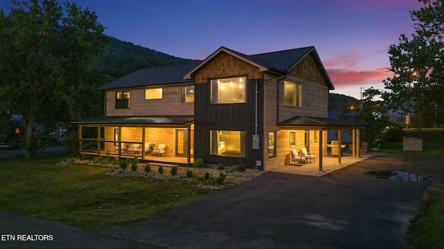 back house at dusk with a porch, a patio, a mountain view, and a lawn