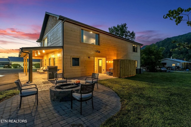 back house at dusk featuring a patio, a yard, and a fire pit