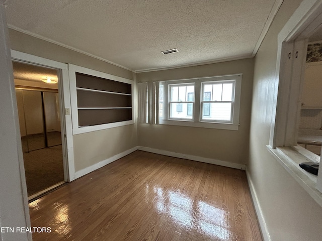 interior space featuring hardwood / wood-style flooring, ornamental molding, a textured ceiling, and built in shelves