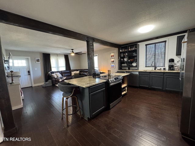 kitchen with a kitchen island, appliances with stainless steel finishes, a breakfast bar area, light stone counters, and dark wood-type flooring