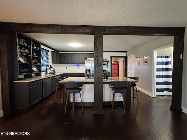 kitchen featuring a breakfast bar area, stainless steel appliances, a center island, light stone counters, and a textured ceiling