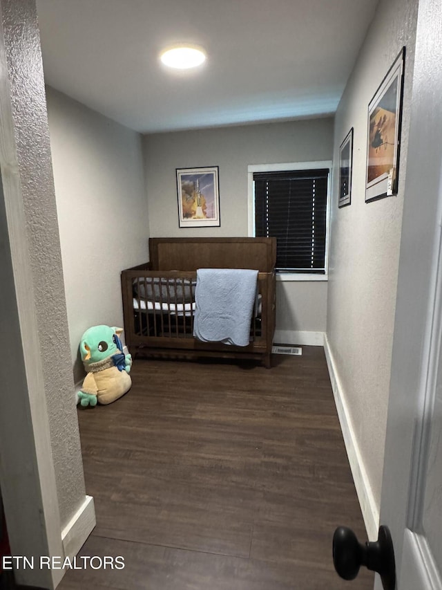 bedroom featuring dark wood-type flooring and a nursery area