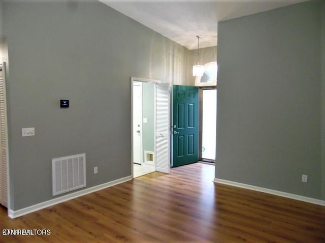 entryway featuring wood-type flooring, a towering ceiling, and an inviting chandelier