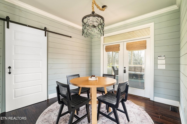 dining space featuring dark hardwood / wood-style flooring, ornamental molding, a barn door, and french doors