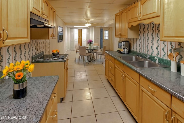 kitchen featuring light tile patterned floors, decorative backsplash, under cabinet range hood, stainless steel gas cooktop, and a sink