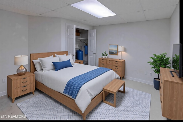 bedroom featuring a closet, baseboards, concrete flooring, and a drop ceiling