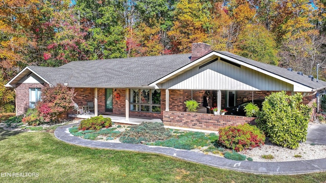 ranch-style house with brick siding, a chimney, roof with shingles, covered porch, and a front yard