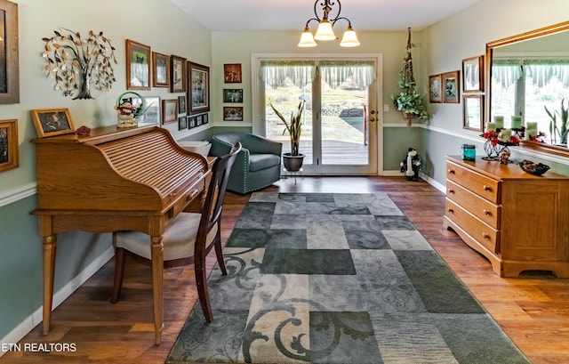 living area with baseboards, plenty of natural light, wood finished floors, and an inviting chandelier