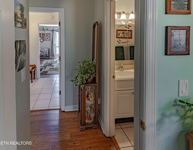 corridor with a sink, wood finished floors, and baseboards