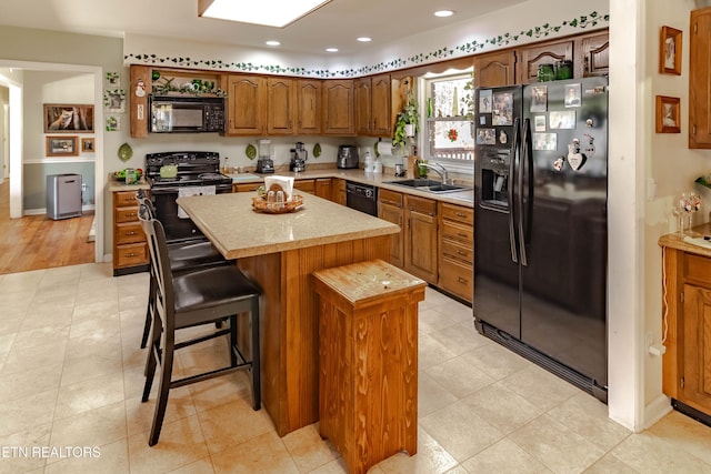 kitchen featuring a sink, a kitchen island, light countertops, black appliances, and brown cabinetry