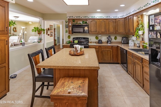 kitchen featuring a breakfast bar area, a sink, light countertops, brown cabinets, and black appliances