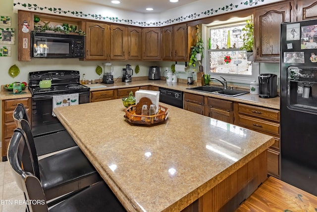 kitchen featuring recessed lighting, a breakfast bar, a sink, a center island, and black appliances