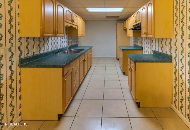 kitchen with light tile patterned floors, a drop ceiling, under cabinet range hood, a sink, and dark countertops