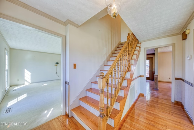 staircase with an inviting chandelier, ornamental molding, hardwood / wood-style floors, and a textured ceiling