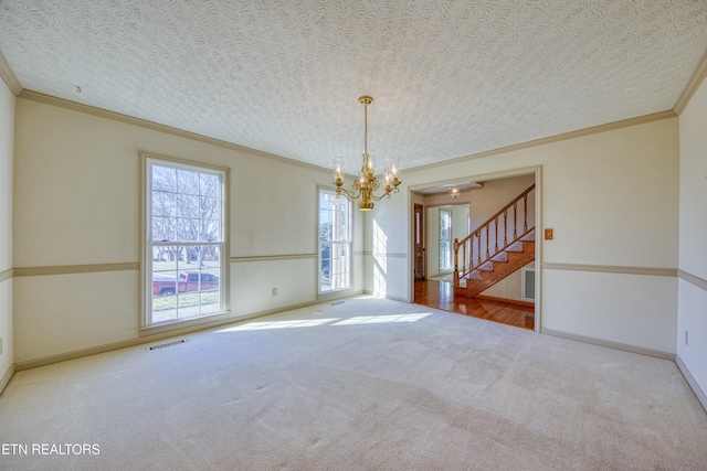 carpeted spare room with ornamental molding, a textured ceiling, and a notable chandelier