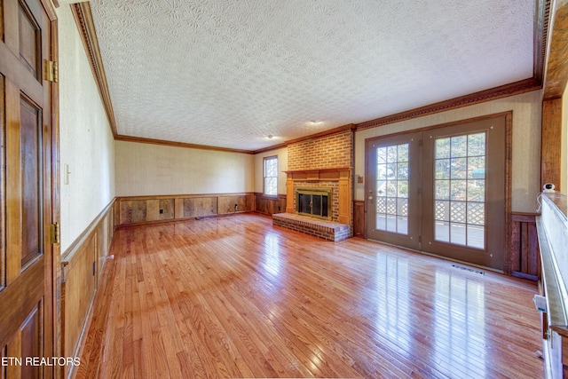 unfurnished living room with crown molding, plenty of natural light, a textured ceiling, and light wood-type flooring