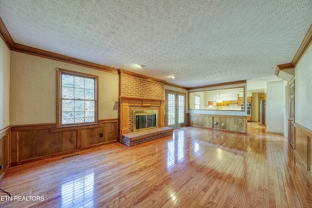 unfurnished living room with ornamental molding, a textured ceiling, a brick fireplace, and light wood-type flooring