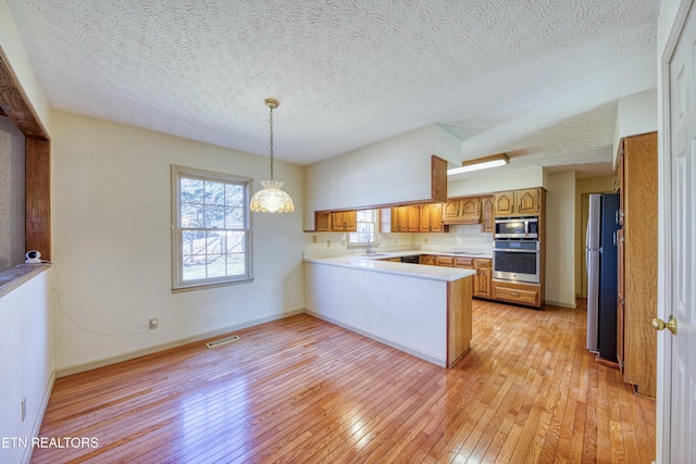 kitchen with sink, decorative light fixtures, light wood-type flooring, appliances with stainless steel finishes, and kitchen peninsula