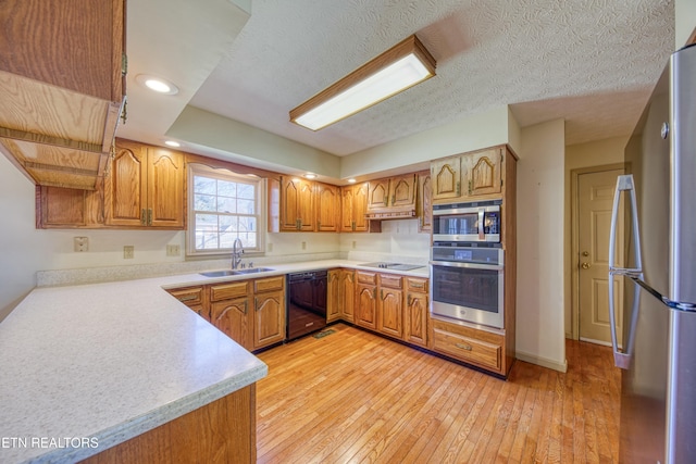 kitchen featuring sink, light hardwood / wood-style flooring, a textured ceiling, and black appliances