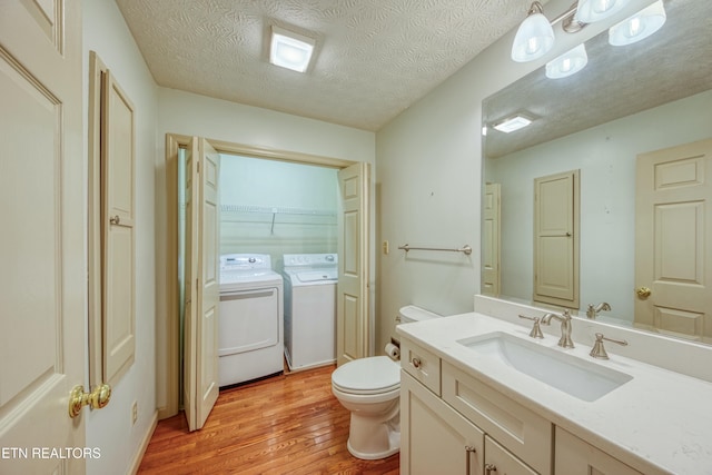 bathroom featuring washer and dryer, hardwood / wood-style floors, vanity, toilet, and a textured ceiling