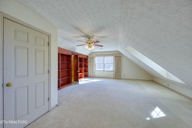 additional living space with ceiling fan, light colored carpet, lofted ceiling with skylight, and a textured ceiling